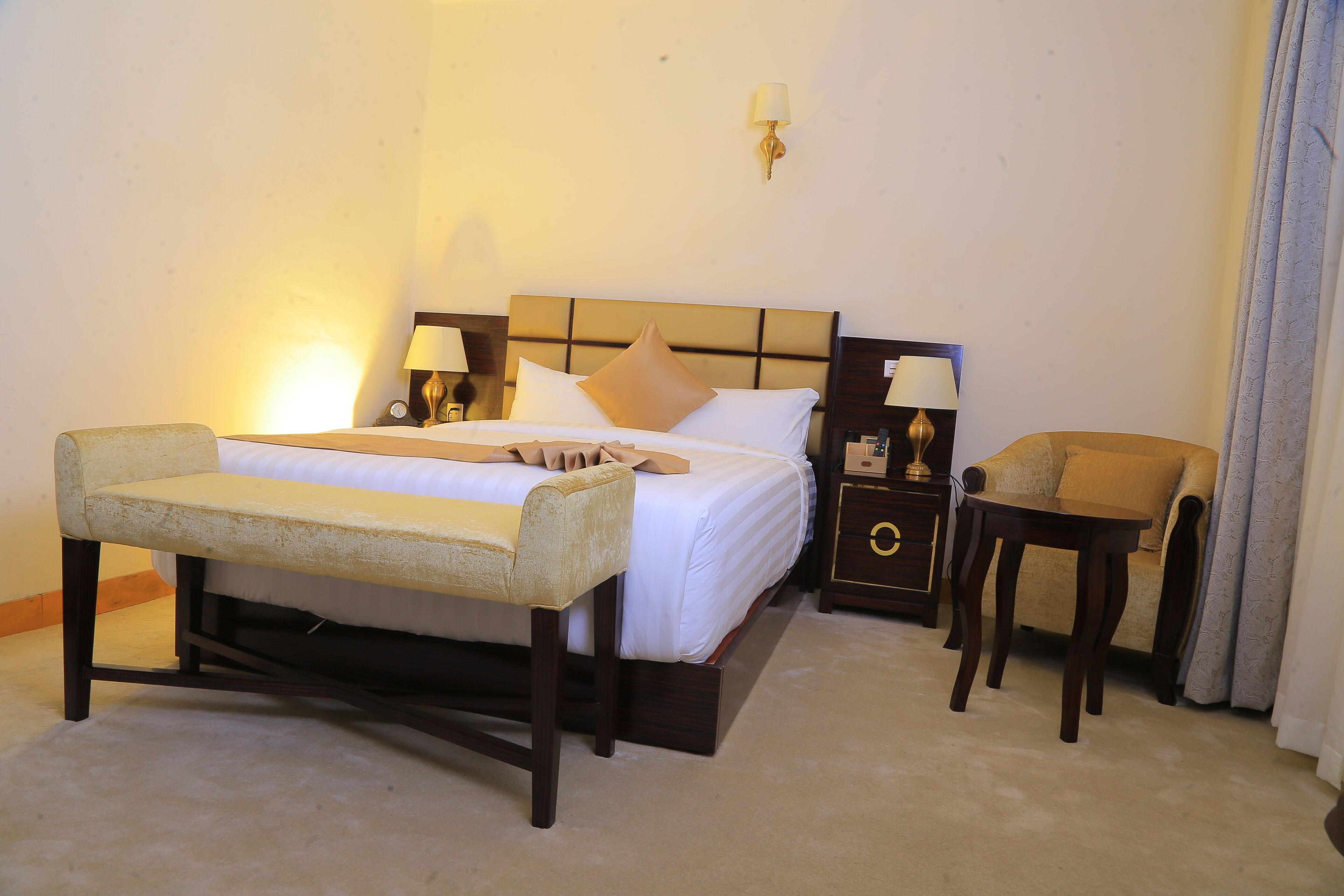 A hotel room with a bed, bedside tables, a bench, a sofa, and a lamp.