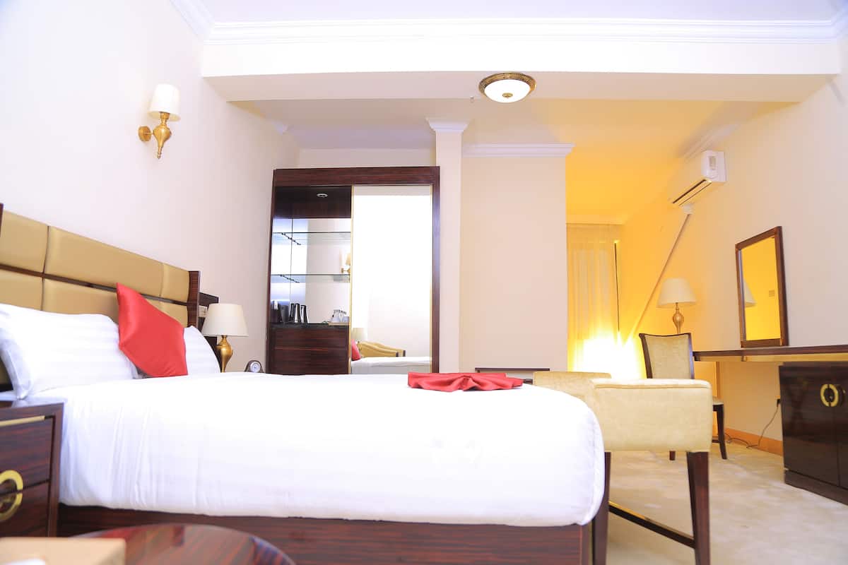 Habitación de hotel con una cama grande, mesitas de noche, un escritorio, una silla, un aparador y un espejo.