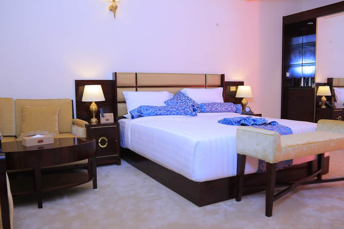 Una habitación de hotel con una cama grande, dos mesitas de noche con lámparas, un sofá y un espejo.