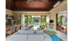Relax in this spacious living area with a sofa, TV, and dining space overlooking a lush garden and pool.