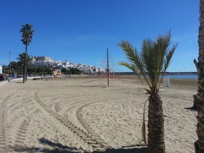 A sandy beach with footprints, palm trees, and a distant building. - Al Andalus Residencial Casa Azahar (Alcala de Xivert)