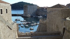 Un pont de pierre historique reliant deux parties d’une ville fortifiée, avec un port rempli de bateaux.