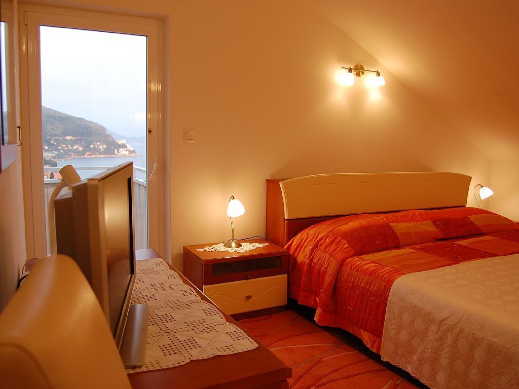 Ein Schlafzimmer mit Bett, Nachttischen, einer Lampe, einem Fenster mit Meerblick und einer Tür.