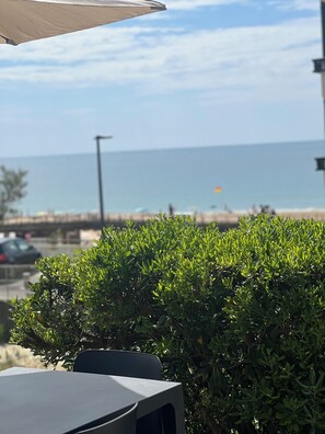 Una mesa y sillas bajo una marquesina, con vista al mar y a la playa de fondo.