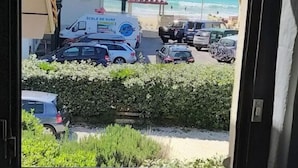 Vista de un estacionamiento con varios coches, una playa y un edificio con un letrero que dice "KCOLE DE SURF".