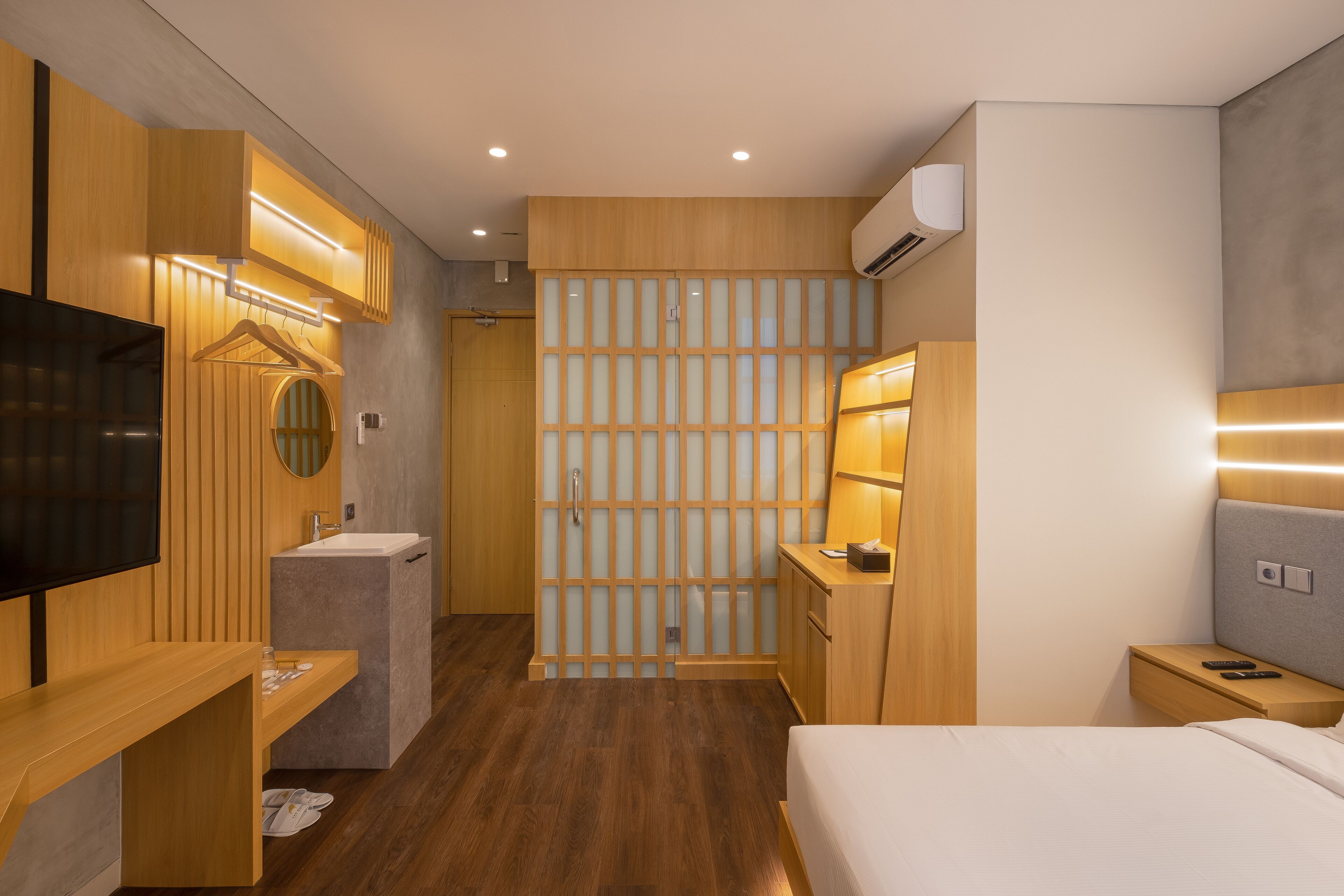 A modern hotel room with a wooden vanity, a flat-screen TV, a bedside table, a bed, and a sliding door leading to a bathroom.