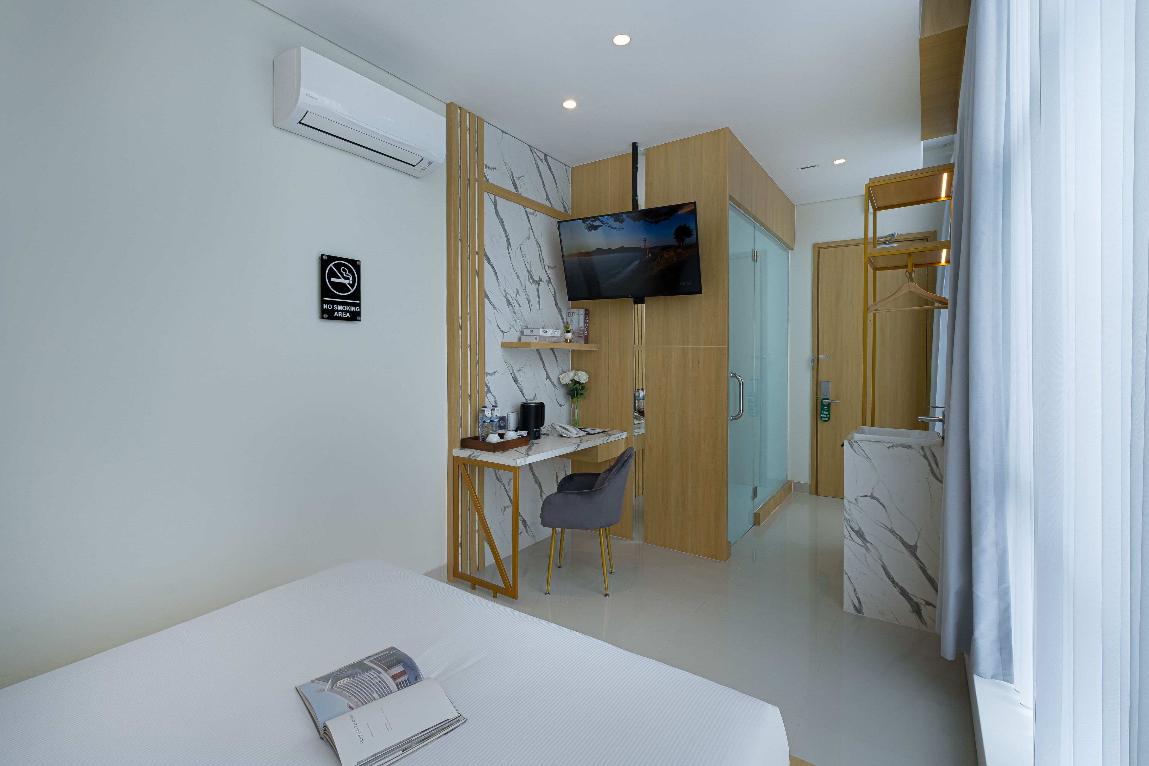 Quarto de hotel com cama, escrivaninha, cadeira, televisão e banheiro com chuveiro e vaso sanitário.