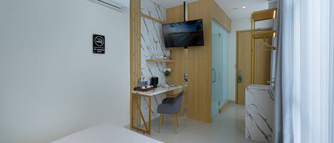 A hotel room with a bed, a desk with a chair, a TV, and a bathroom with a shower and toilet.