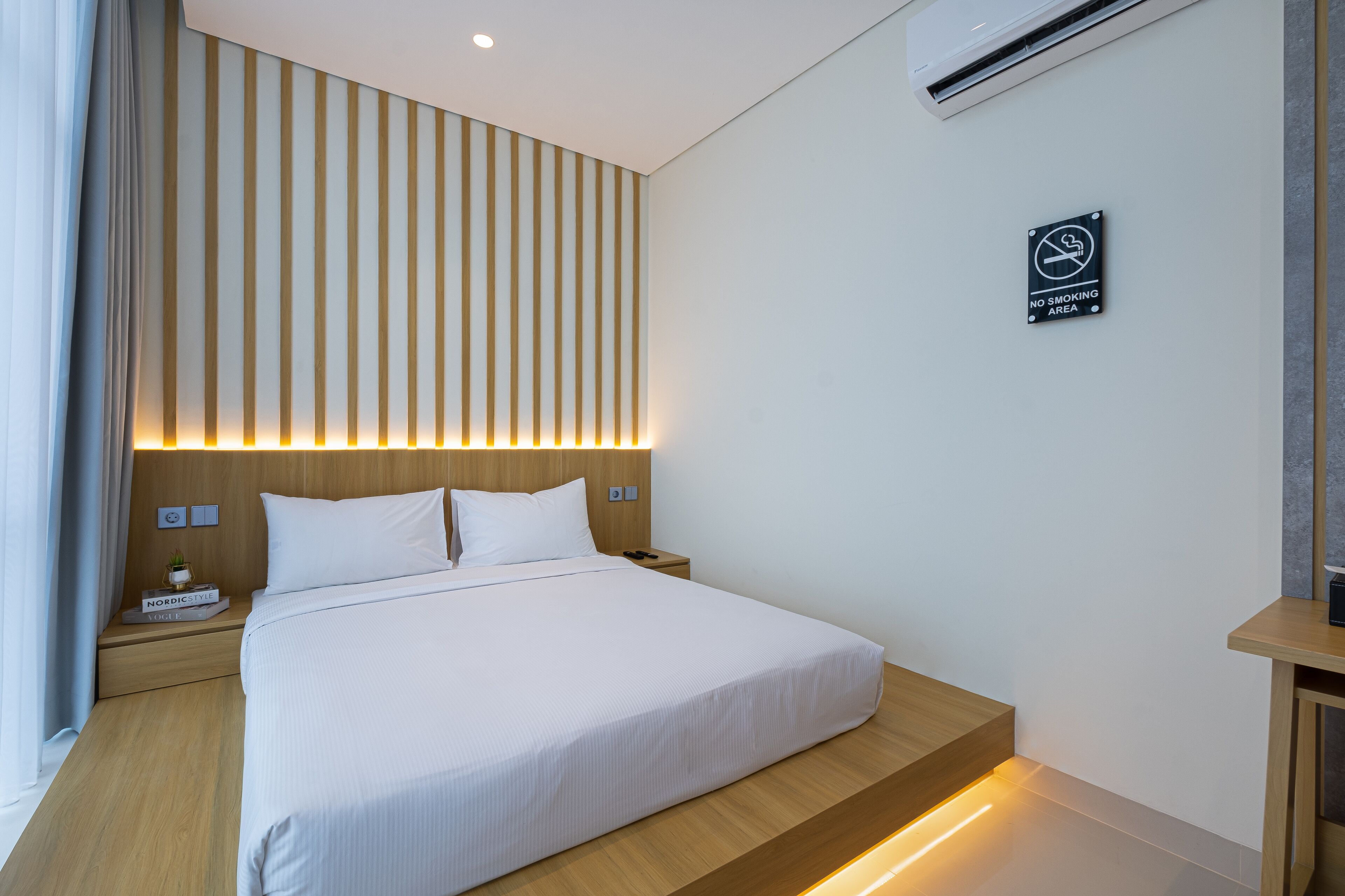 Una habitación de hotel moderna con una cama grande, una mesita de noche y un cartel que indica 