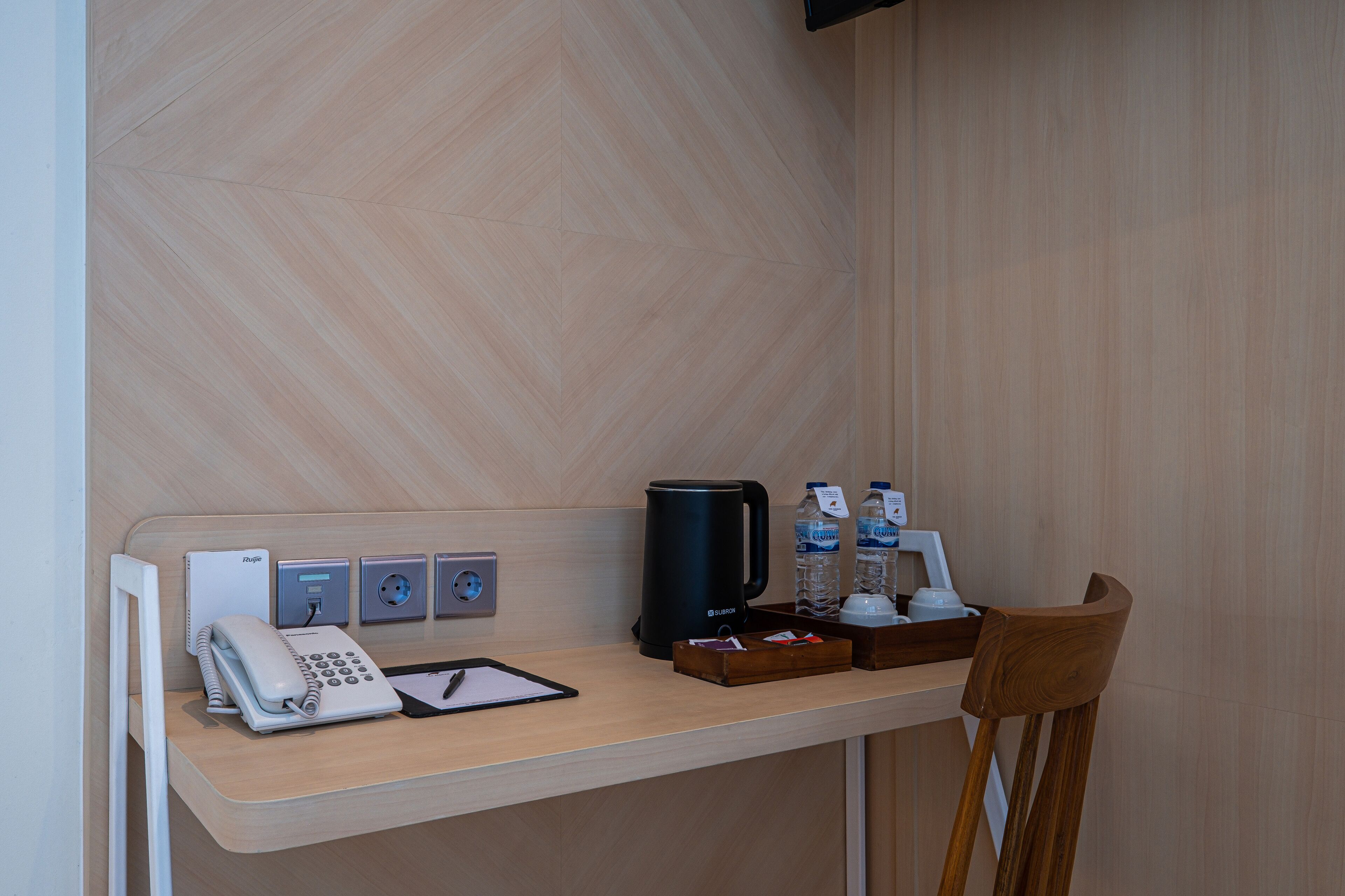 Habitación de hotel con escritorio de madera, teléfono, cafetera y dispensador de agua.