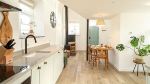 A modern kitchen with a central island, a built-in oven, and a wooden backsplash. - Wensum Spring (Dereham)