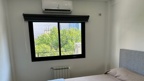 Ein Schlafzimmer mit großem Fenster, Heizkörper und einem Bett mit grauem Kopfteil.