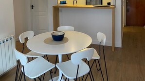 Ein moderner Essbereich mit einem runden Tisch, weißen Stühlen, einer Chandelierleuchte und einer Küche im Hintergrund.