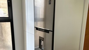 Ein Edelstahl-Kühlschrank steht in einer Ecke eines Raumes mit weißen Wänden und einem Fenster.