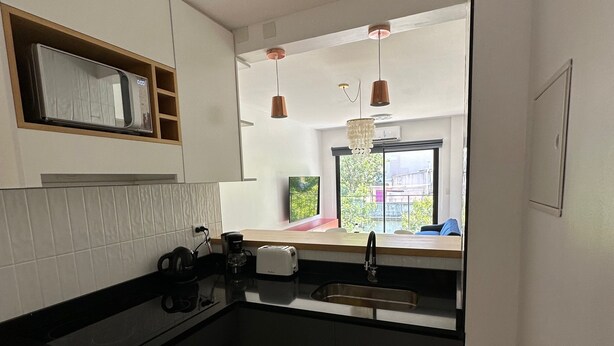 Eine kleine Küche mit schwarzem Arbeitsplatz, einem eingebauten Backofen und einem Spülbecken. Ein Fenster bietet einen Blick nach draußen.