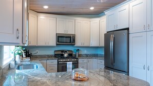 A modern kitchen with white cabinets, a stainless steel refrigerator, a microwave, and a granite countertop.
