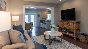 A living room with a sofa, a coffee table, a TV, and a kitchen in the background.