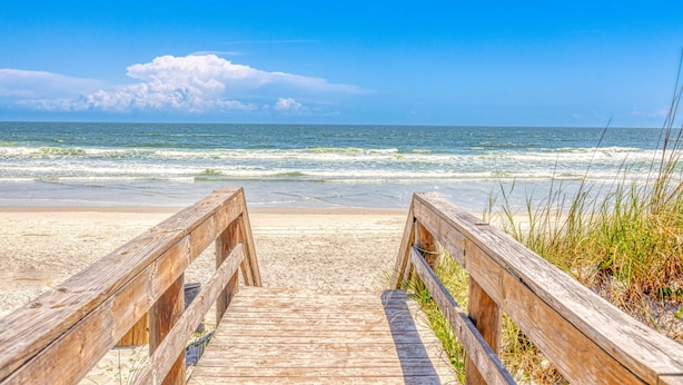 A wooden boardwalk leading to a sandy beach with the ocean in the background.