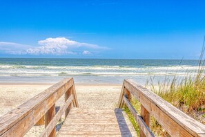 A wooden boardwalk leading to a sandy beach with the ocean in the background.