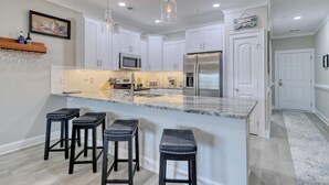 A modern kitchen with white cabinets, a large island with bar stools, stainless steel appliances, and pendant lighting. - Links And Shore 406: 4  BR, 3  BA Condominium in Garden City, Sleeps 12 (Garden City)