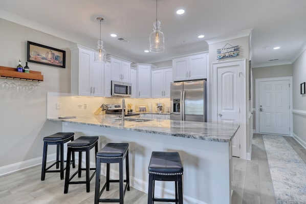 A modern kitchen with white cabinets, a large island with bar stools, stainless steel appliances, and pendant lighting.