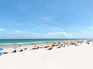 A beach with rows of sun umbrellas and lounge chairs, a clear sky, and the ocean in the background.