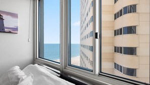 Une chambre d’hôtel dotée d’une grande fenêtre donnant sur la plage et un immeuble de grande hauteur.
