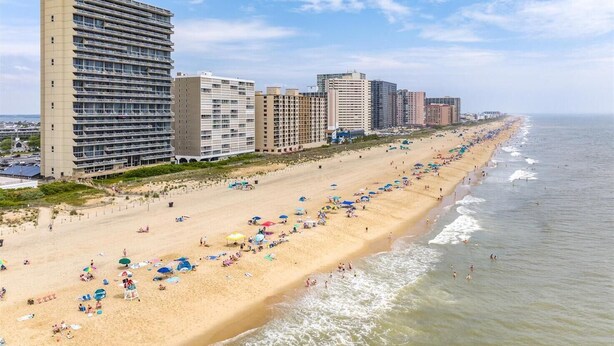 Een strand met meerdere hotelgebouwen langs de kust, voorzien van balkons en een zandstrand met parasols en mensen.
