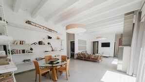 A spacious living area with a glass dining table surrounded by wooden chairs, a sofa, and a coffee table. Shelves with books and decorative items line the walls. - Villa Bohème-chic-Villa-Private Bathroom-Deluxe (Bonifacio)