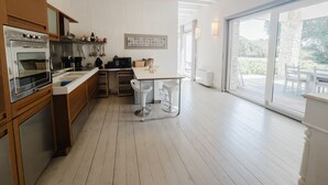 A modern kitchen with wooden cabinets, stainless steel appliances, and a large window offering a view of the outdoors. - Villa Bohème-chic-Villa-Private Bathroom-Deluxe (Bonifacio)
