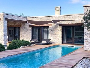 Una casa moderna con piscina, paredes de piedra y ventanas amplias.