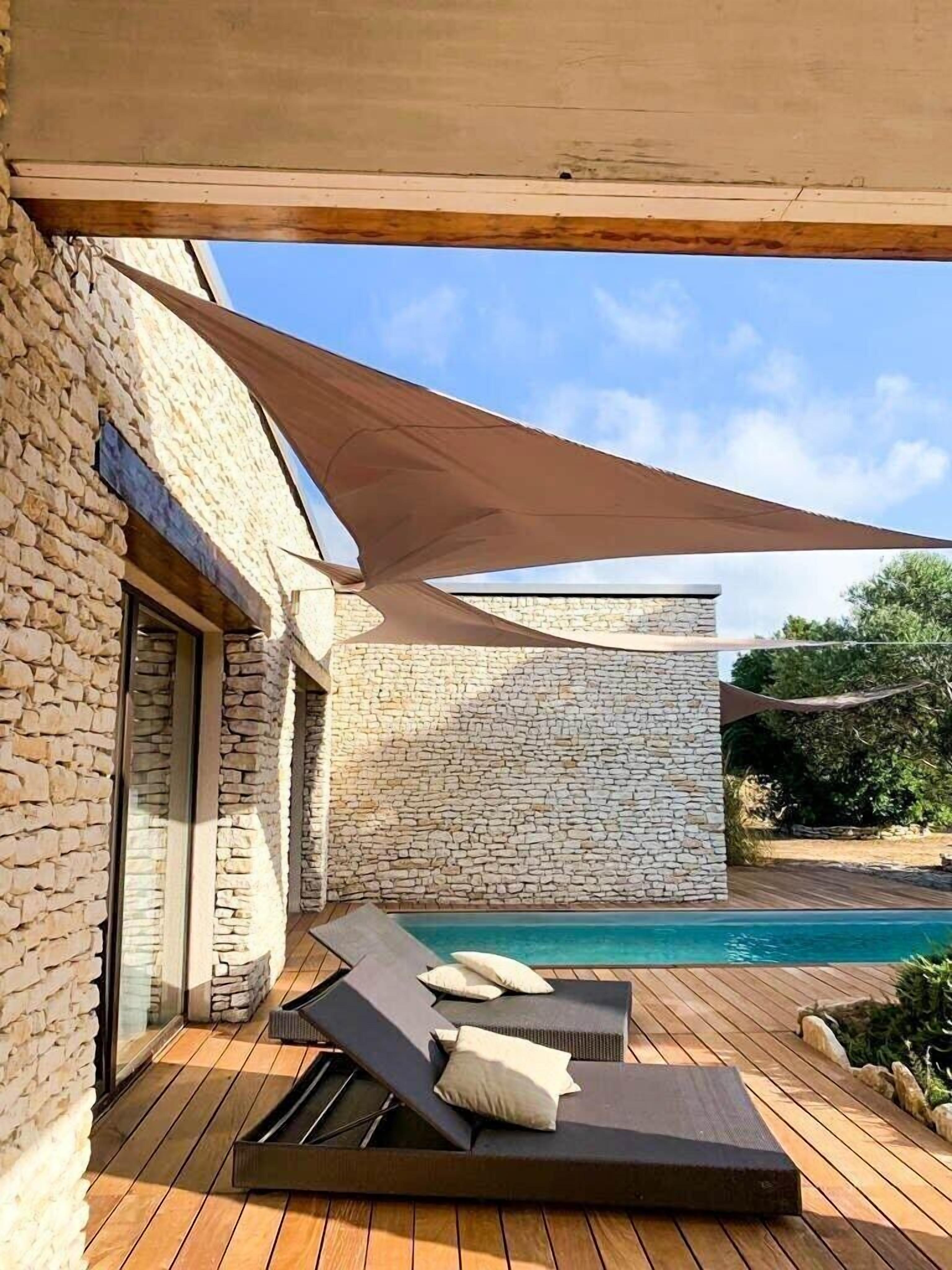 Uma área de piscina moderna ao ar livre, com paredes de pedra, deck de madeira e espreguiçadeiras.