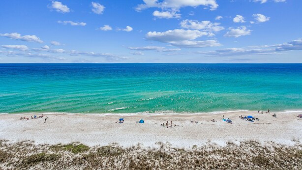 Ein Strand mit klarem türkisblauem Wasser und weißem Sand, mit mehreren Sonnenschirmen und entspannten Personen.