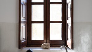 Una cocina con un lavamanos doble, una ventana con contraventanas abiertas y una piedra en el alféizar.