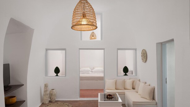 Una sala de estar moderna con un sofá blanco, una mesita de centro y una lámpara colgante grande de fibras naturales. Hay tres cuadros enmarcados en la pared, un pequeño árbol decorativo y una alfombra redonda de fibras naturales.