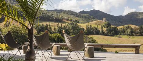 A wooden deck with hammocks and benches, overlooking a hilly landscape.