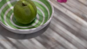 Et grønt æble på en stribet tallerken på et bord.