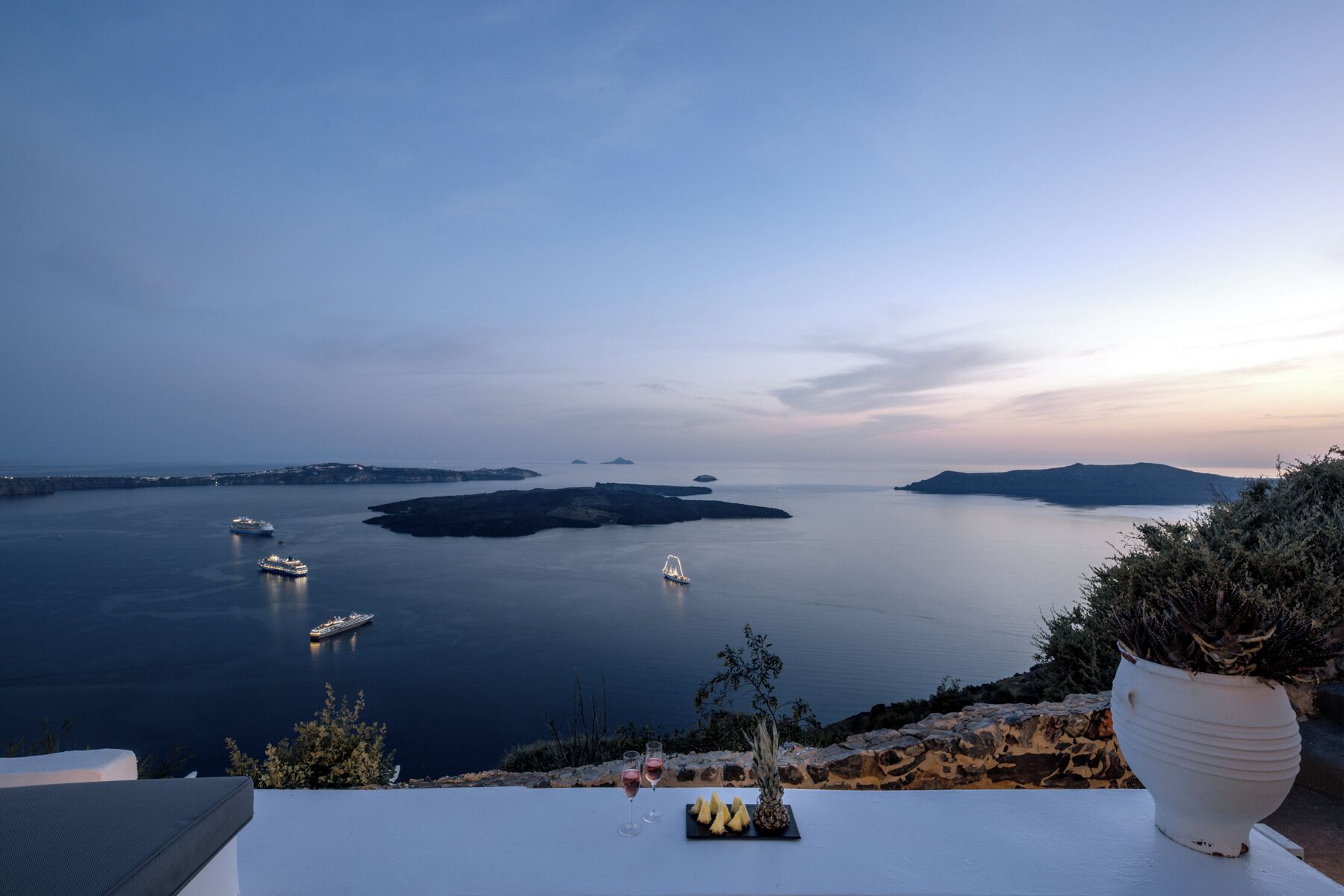 A seaside view with a table set for dining, overlooking calm waters and distant islands.