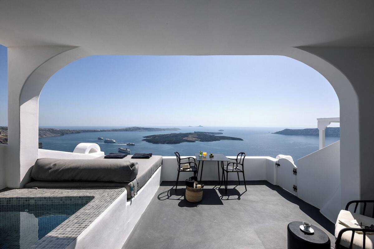 A balcony with a view of the sea, a table with chairs, and a small pool.