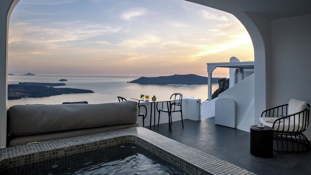 A modern outdoor seating area with a view of the sea and islands at sunset. - WeSense by Caldera Houses (Santorini)