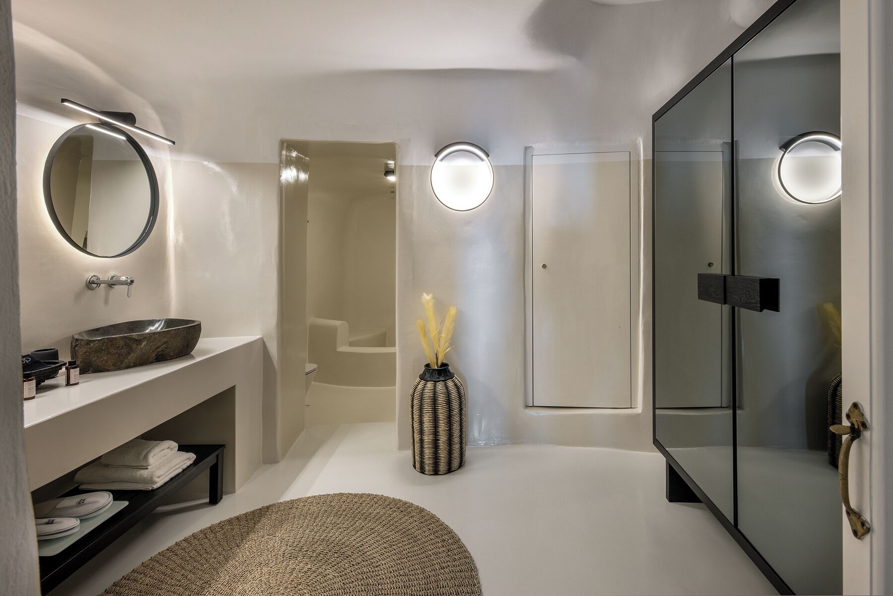 A modern bathroom with a large mirror, a round sink, a glass shower enclosure, and a walk-in shower.