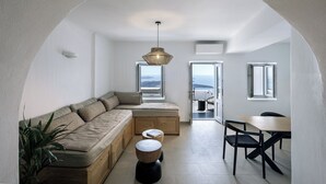 A modern living room with a sofa, a dining table, and chairs. There is a view of the sea through large windows. - WeSense by Caldera Houses (Santorini)