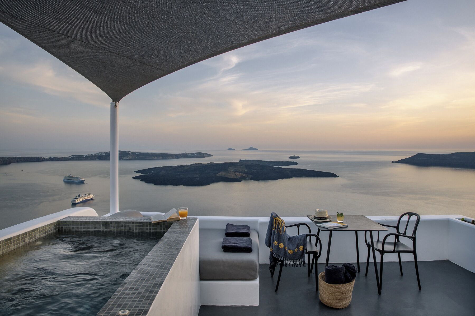 A terrace with a view of the sea, a hot tub, seating, and a table with drinks.