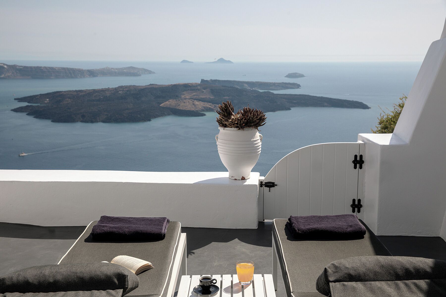 A balcony with a view of the sea, a white vase with plants, and two lounge chairs with towels.