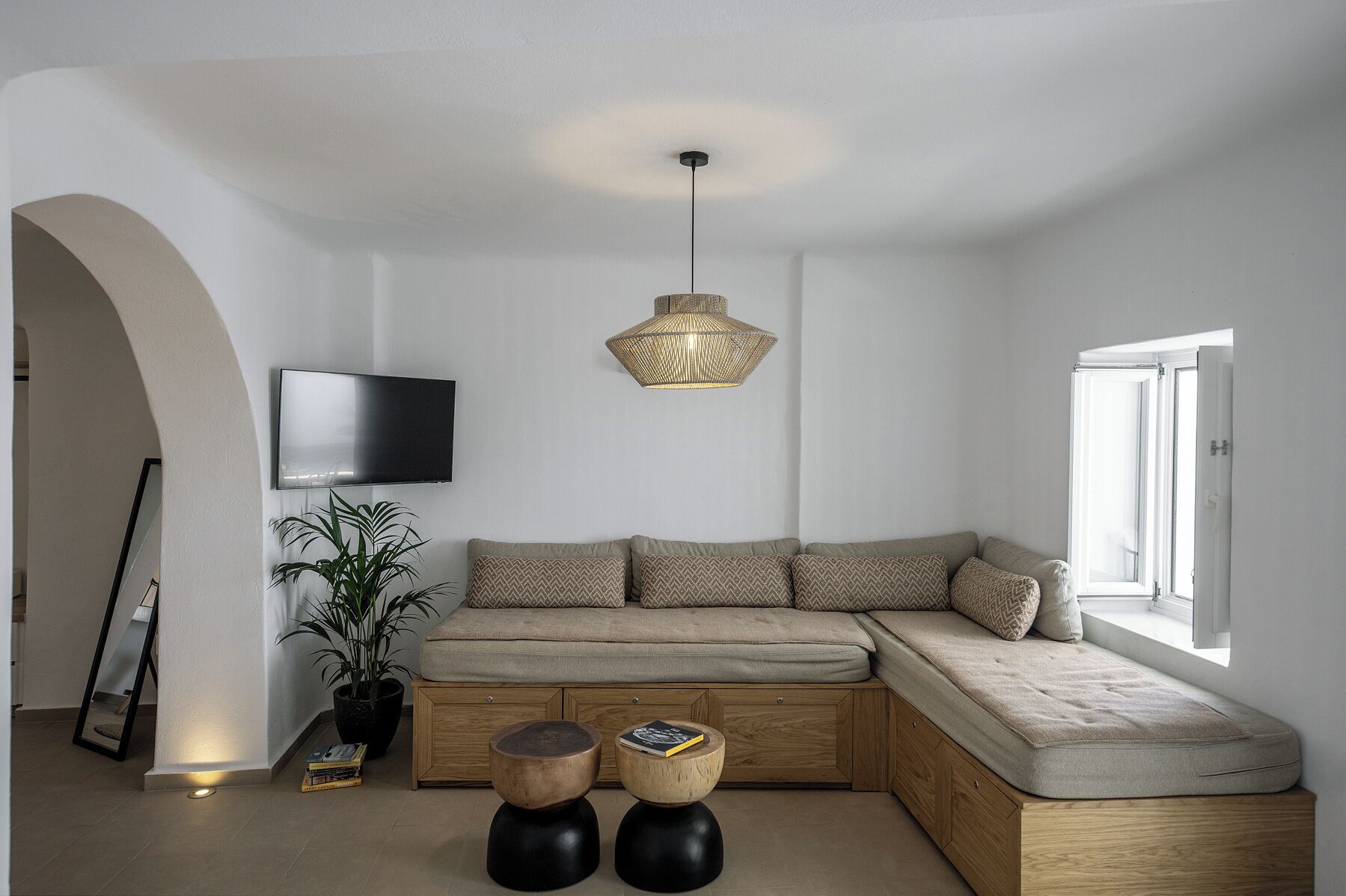 A modern living room with a built-in L-shaped sofa, a large flat-screen TV, a unique woven pendant light, and a potted plant.