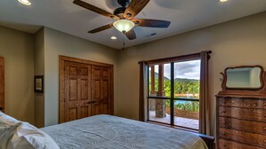 Une chambre à coucher avec un lit, une armoire en bois, un ventilateur de plafond et une fenêtre donnant sur un paysage verdoyant.