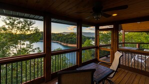 Une terrasse en bois avec une table et des chaises, offrant une vue sur un lac et des collines boisées.
