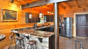 L’intérieur d’une cabane en bois est agrémenté d’un bar central en pierre, de meubles de rangement en bois foncé et d’un grand réfrigérateur.