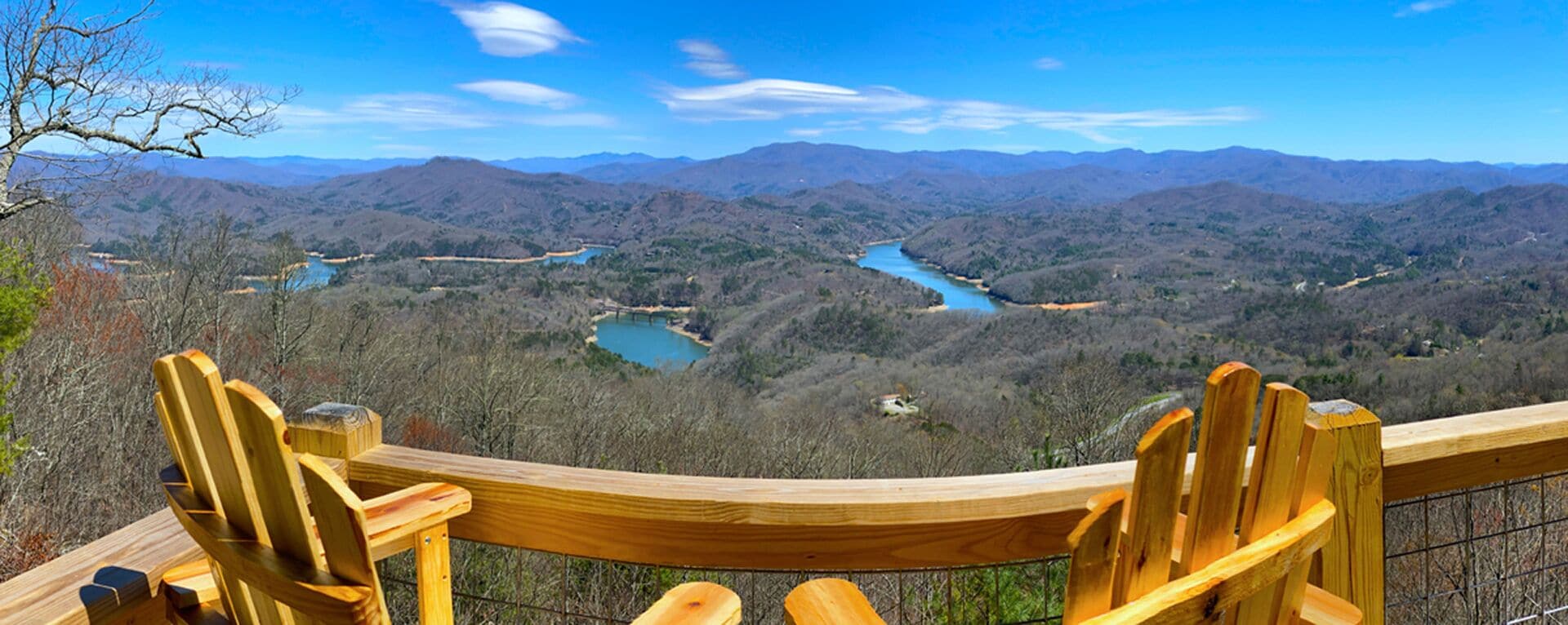 A wooden deck with chairs overlooking a mountainous landscape with a river.