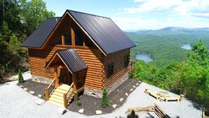 Une cabane en rondins avec un toit en pente, une véranda et une vue sur un lac et des montagnes.